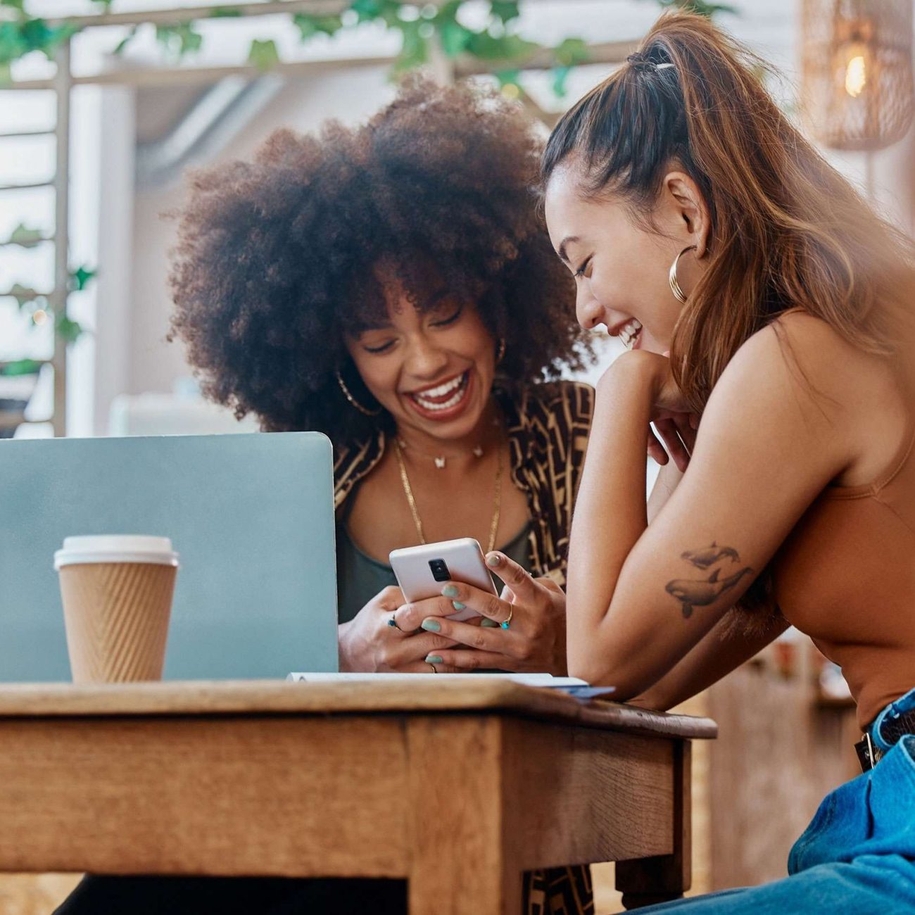 Two friends shopping online over a smartphone at brunch.